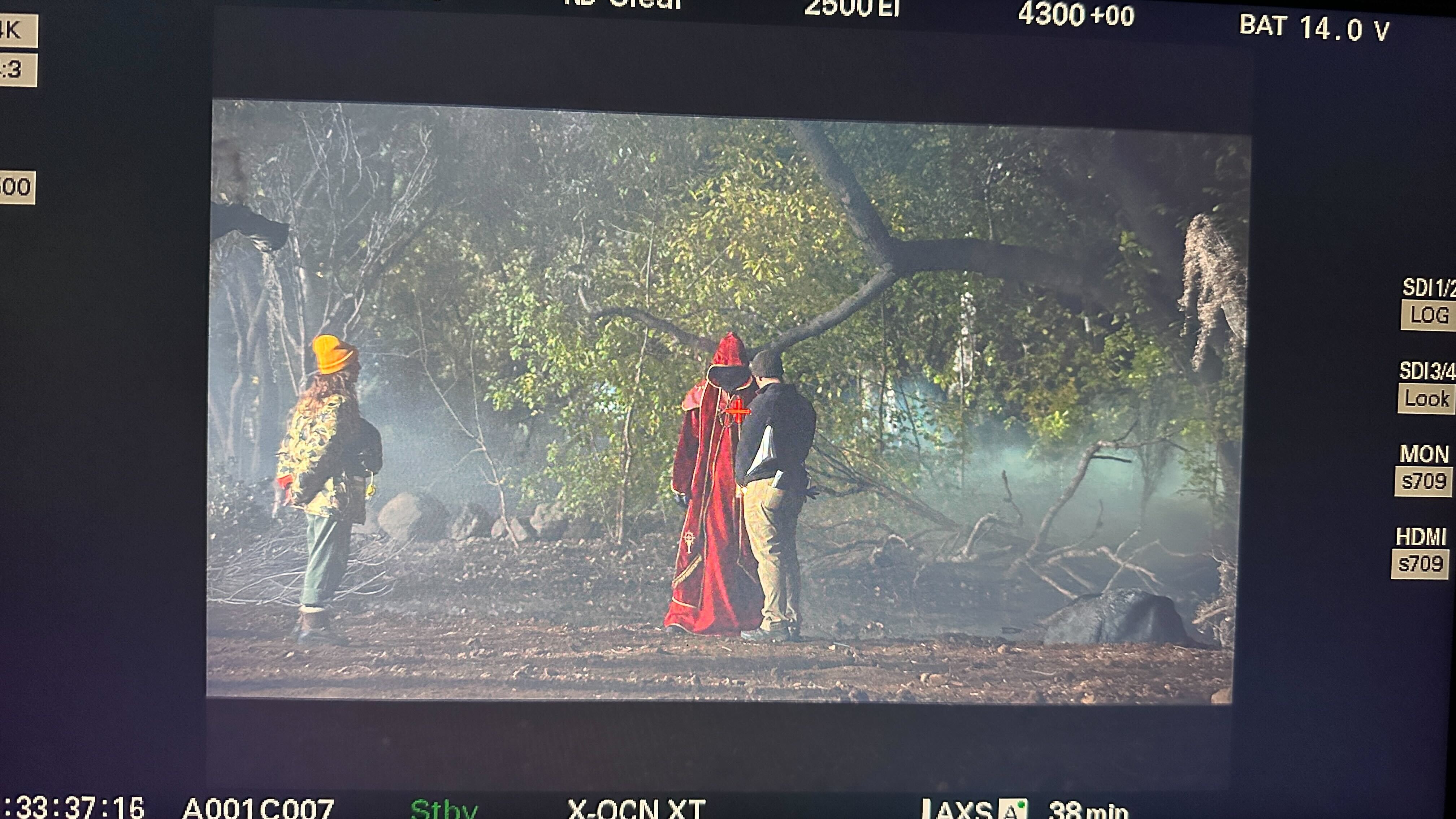 Camera monitor showing crew and a red-robed Diablo performer rehearsing in the forest