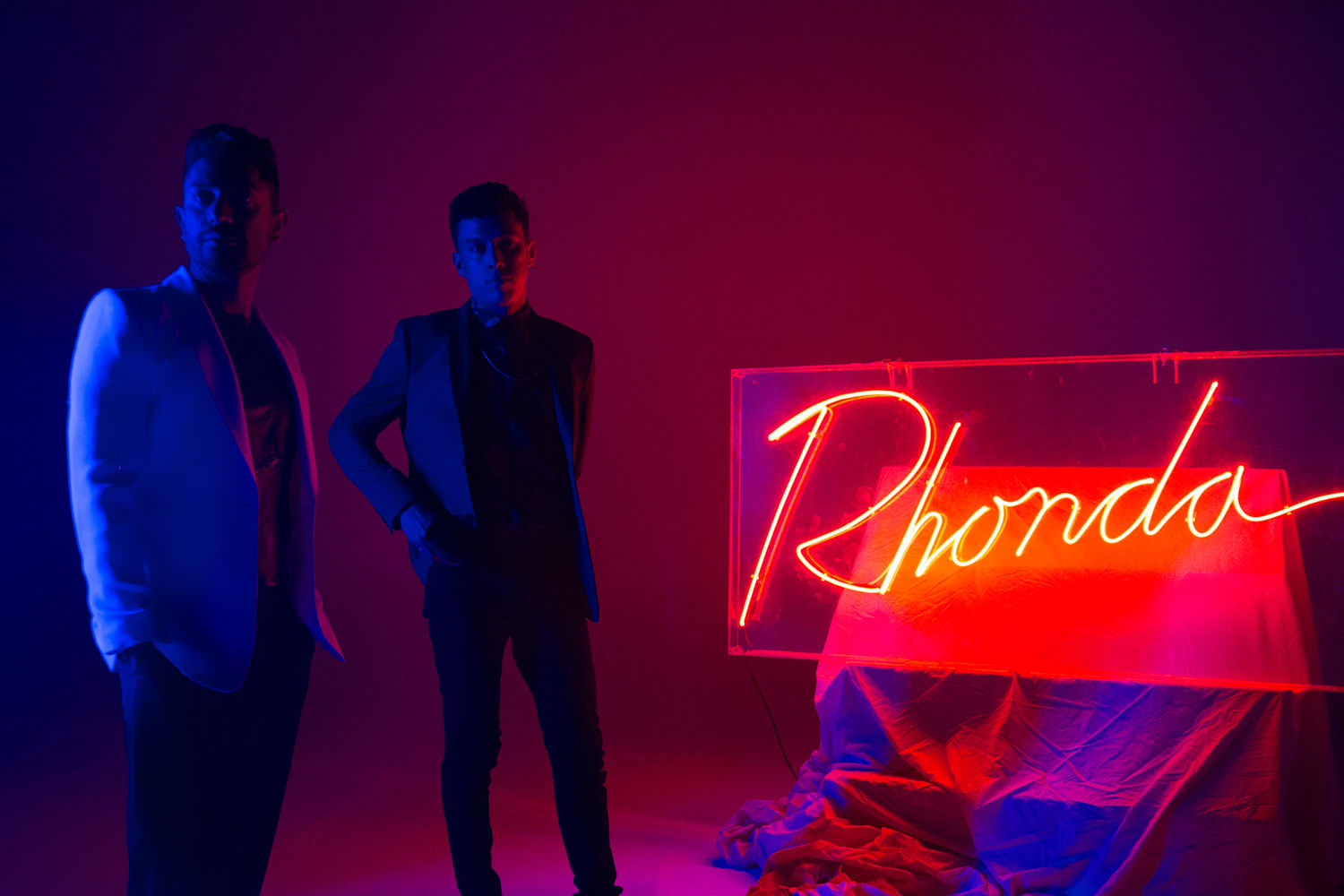 Two people beside the glowing Rhonda neon sign